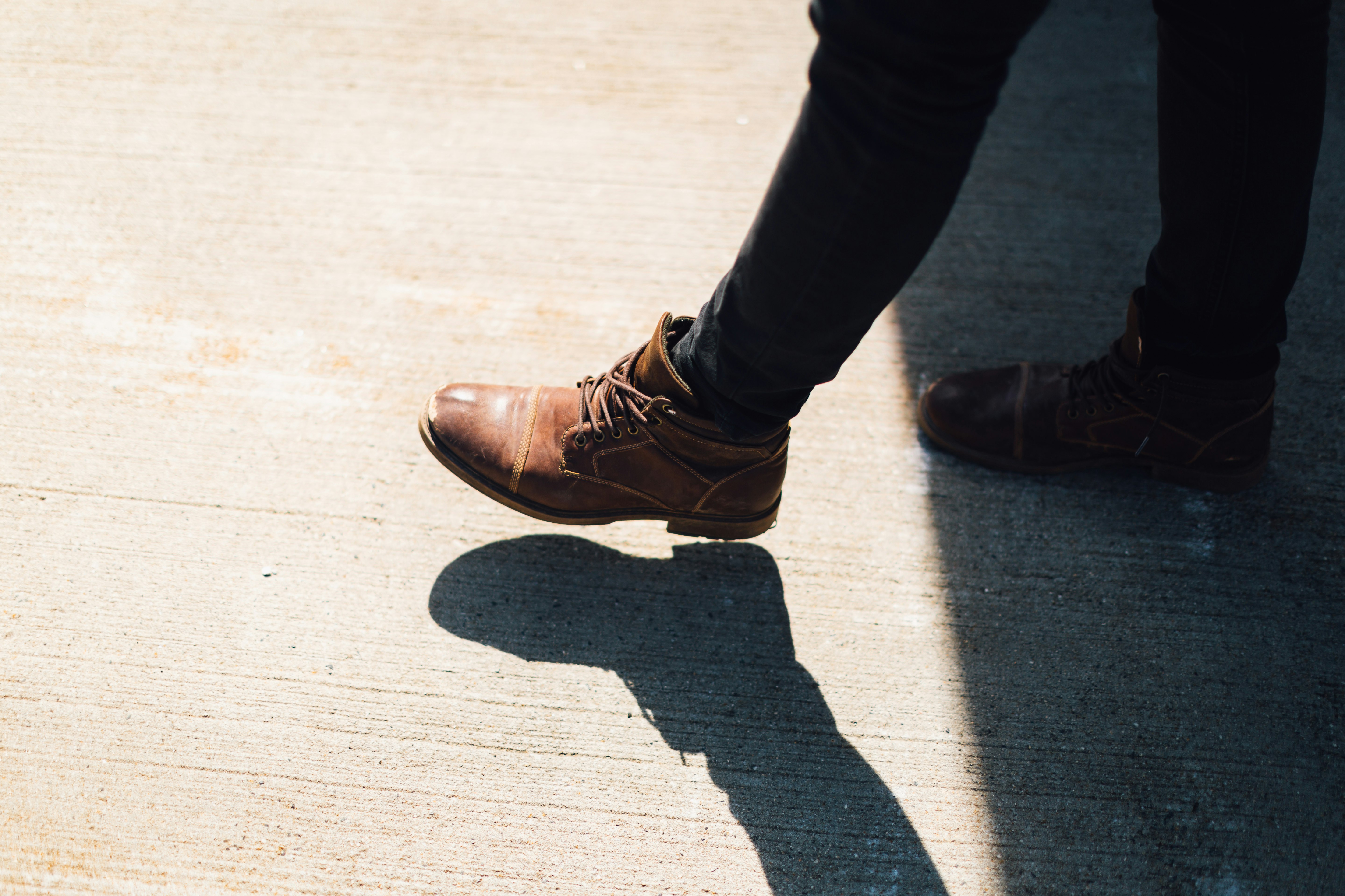 person wearing brown leather boots walking on gray concrete during daytime